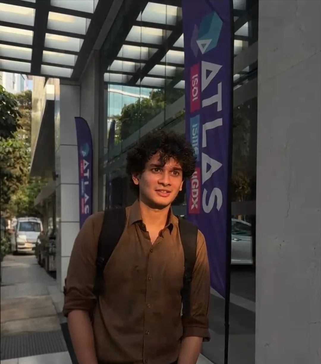 Keenan smiling in a brown shirt outside Atlas SkillTech University at golden hour